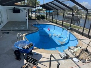 Backyard pool under construction with blue water, fence, and tools on the patio