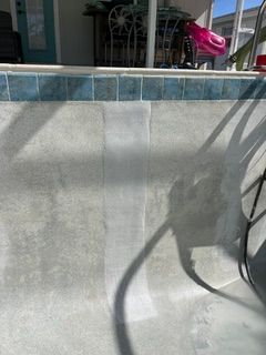 Empty concrete pool wall with blue tile border and shadows from patio furniture
