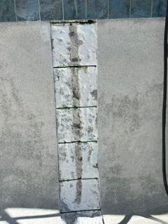 Weathered concrete wall with a narrow vertical strip of peeling white paint and dark stains.