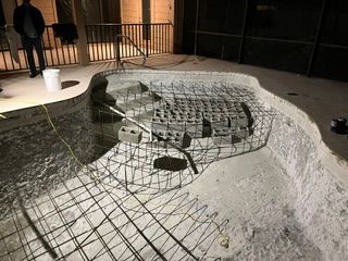 Wireframe model of a large amphitheater or stadium site, showing curved seating layout in a sandy excavation area.