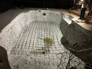 Drained concrete swimming pool with exposed rebar mesh, viewed indoors under construction lights