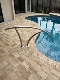 Curved stainless-steel pool handrail beside a tiled patio and blue swimming pool