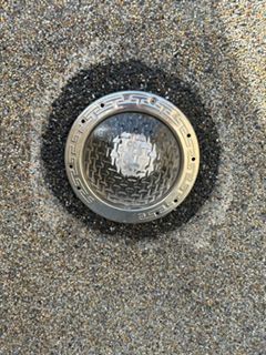 Round metal wall light on a textured gray surface, with a dark circular stain around it