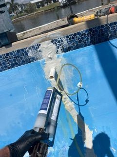 Gloved hand applying pool sealant near a blue tiled pool edge with water splashing above the surface