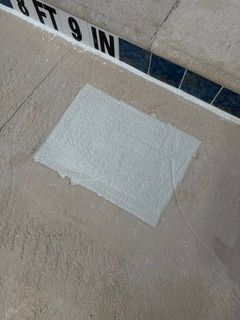 White patch of tape on beige concrete near a tiled pool edge with partial “NO DIVING” sign visible