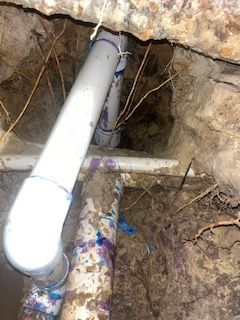 White PVC pipe in an excavated dirt trench beside a rock wall.
