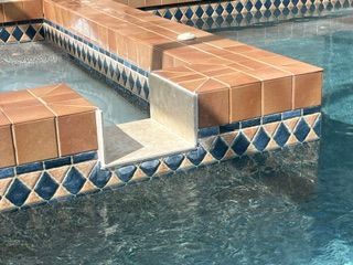 Tiled pool ledge and steps beside blue water with geometric border tiles