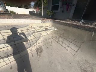 Shadow of a person beside a bent wireframe structure on a sunlit concrete patio