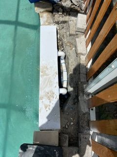 Pool edge with exposed white plumbing pipes beside a wooden deck and green pool water.