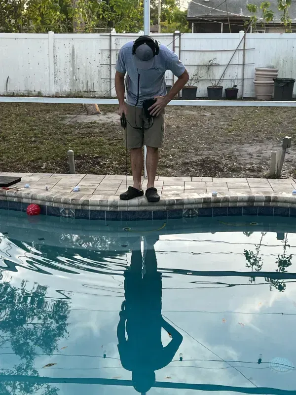 Person standing on pool edge, looking down at the water with a reflection below.