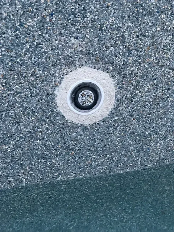 Close-up of a round metal drain or fixture set into a textured gray-blue surface.