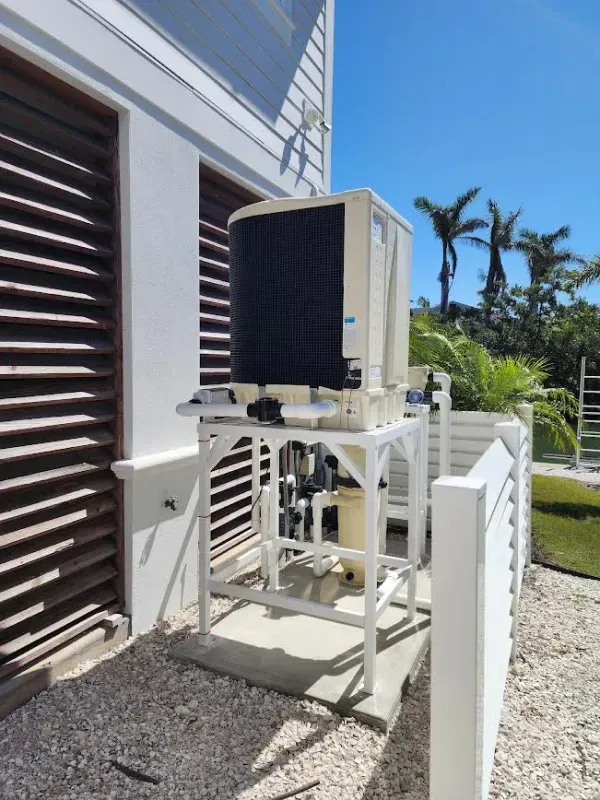 Outdoor air conditioning unit mounted on a metal platform beside a building, with palm trees in the background