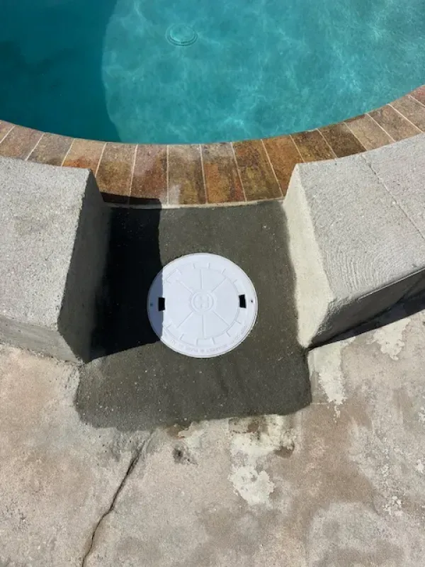 Pool deck drain cover beside blue swimming pool water