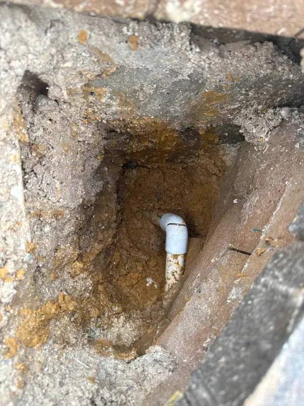 Close-up of a rough stone hole with a white pipe protruding from the center.