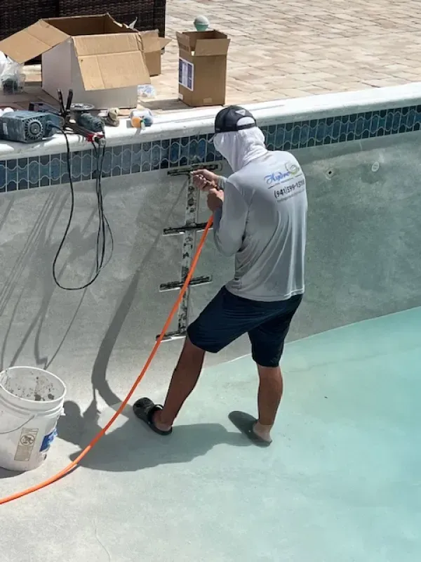 Worker spraying pool interior with a hose, standing in an empty swimming pool.
