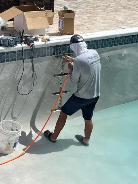 Worker spraying pool interior with a hose, standing in an empty swimming pool.