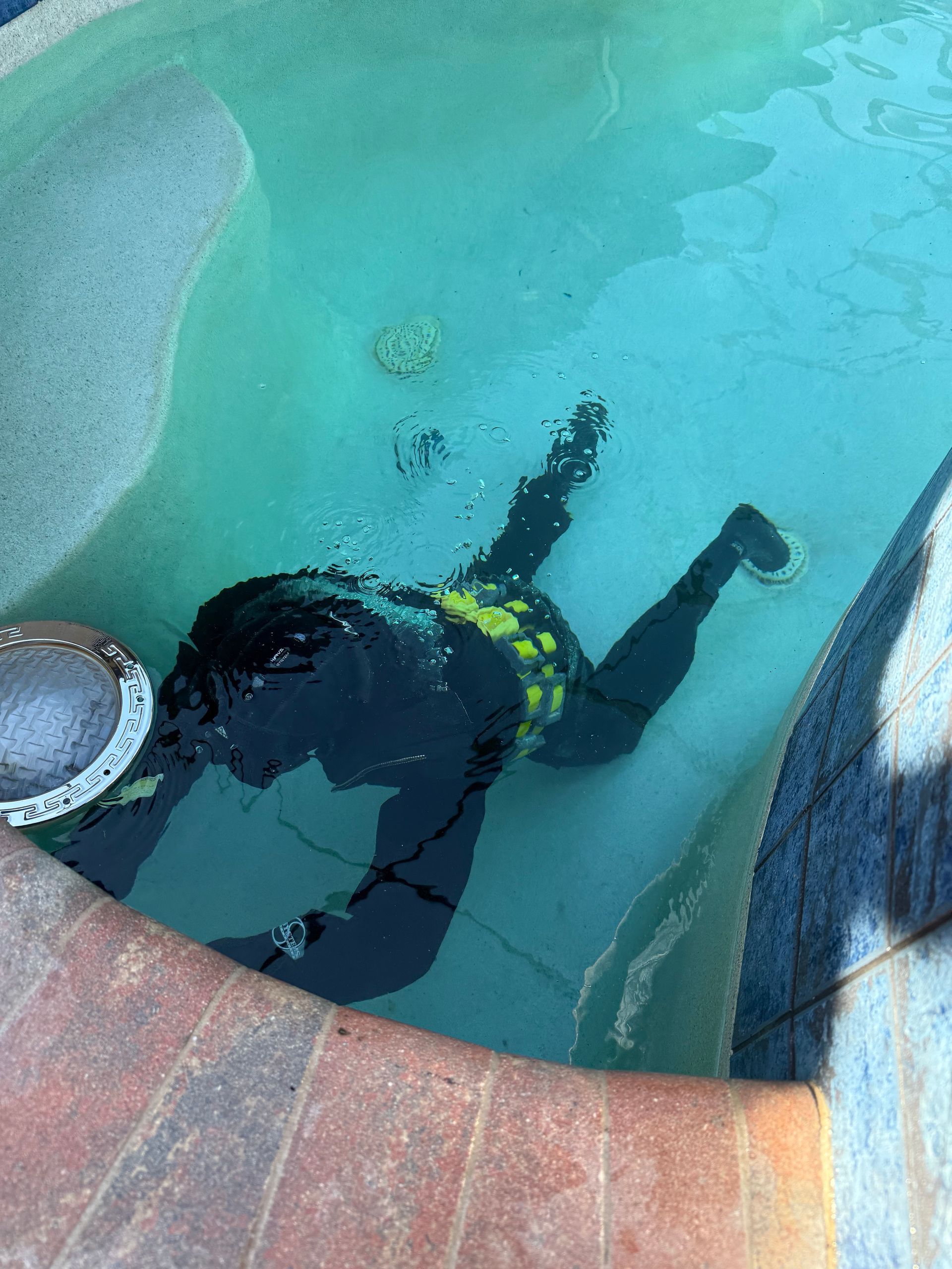 Diver in black gear floating in a clear turquoise pool beside a stone edge