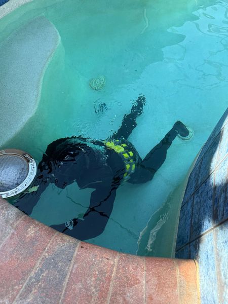 Person in scuba gear floating in a turquoise pool beside a curved tiled edge.
