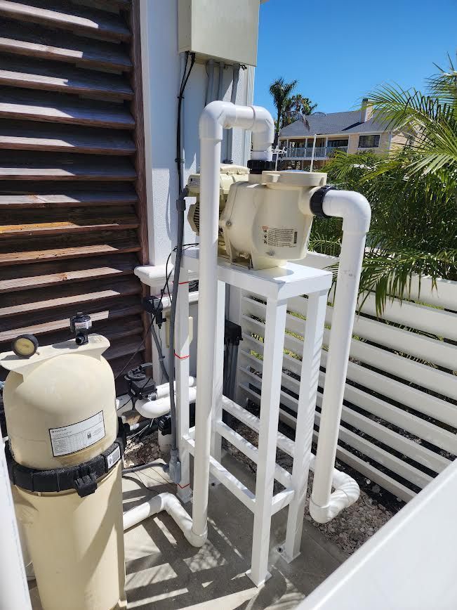 Outdoor pool equipment with beige filtration tanks and white PVC pipes beside a building.
