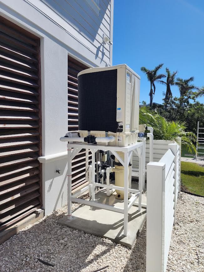 Outdoor HVAC unit beside a white house wall with louvered vents and palm trees in the background
