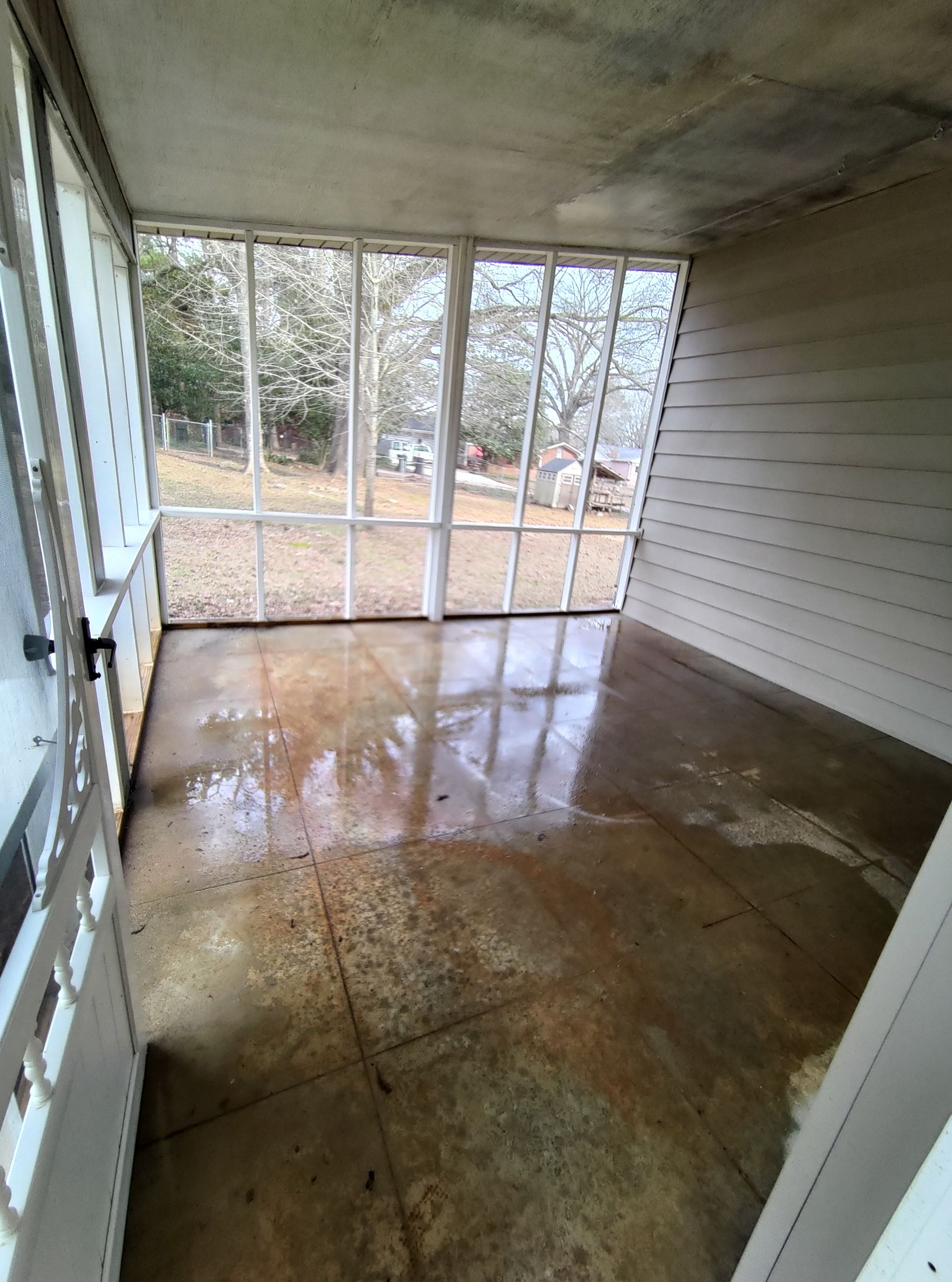 Een afgeschermde veranda met veel ramen en een betonnen vloer.
