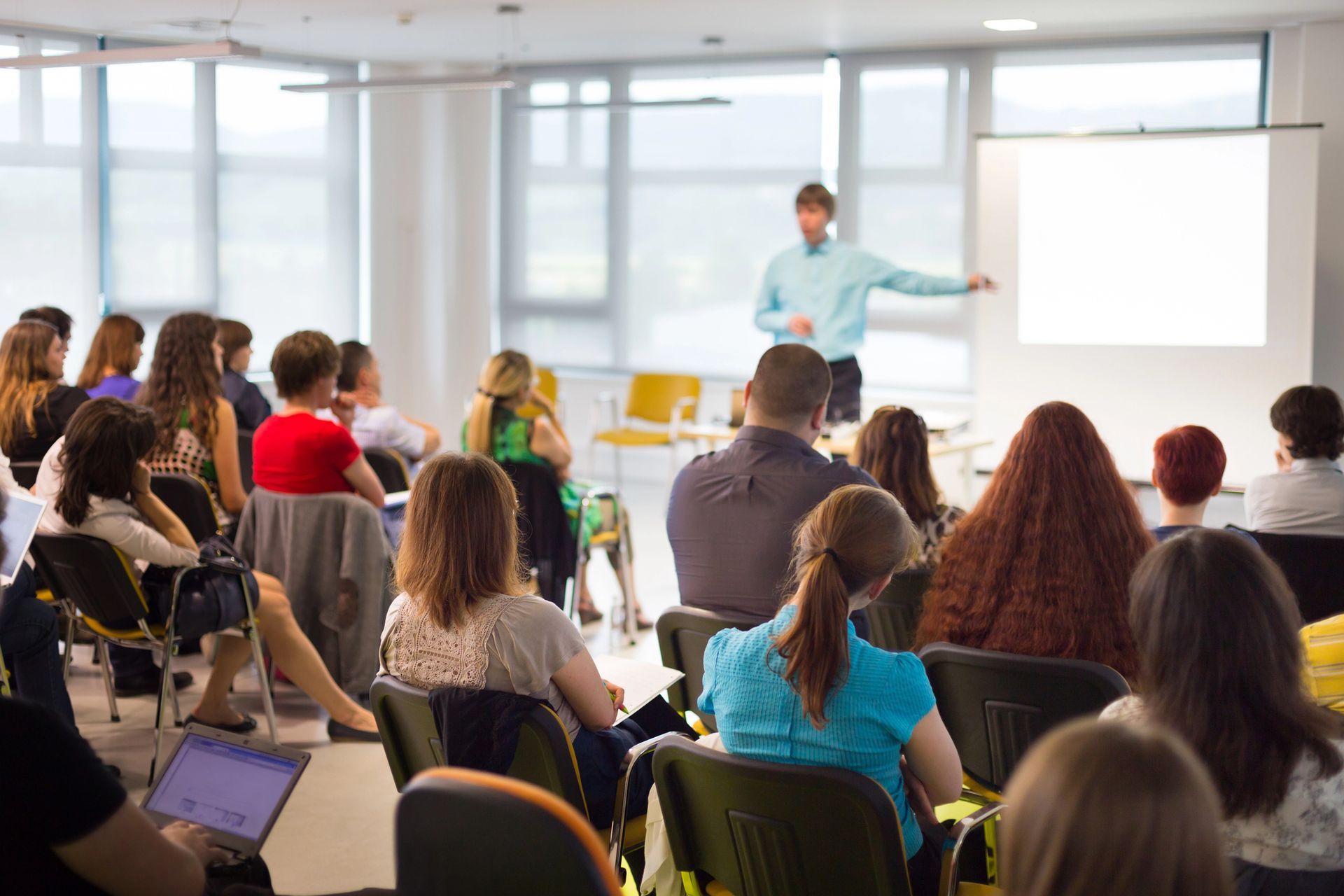 Relatore che si rivolge a un pubblico seduto in una luminosa sala conferenze.