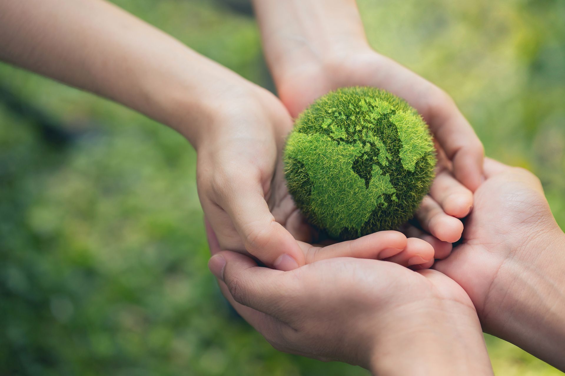 Mani che reggono una piccola sfera ricoperta di muschio verde all'aperto.