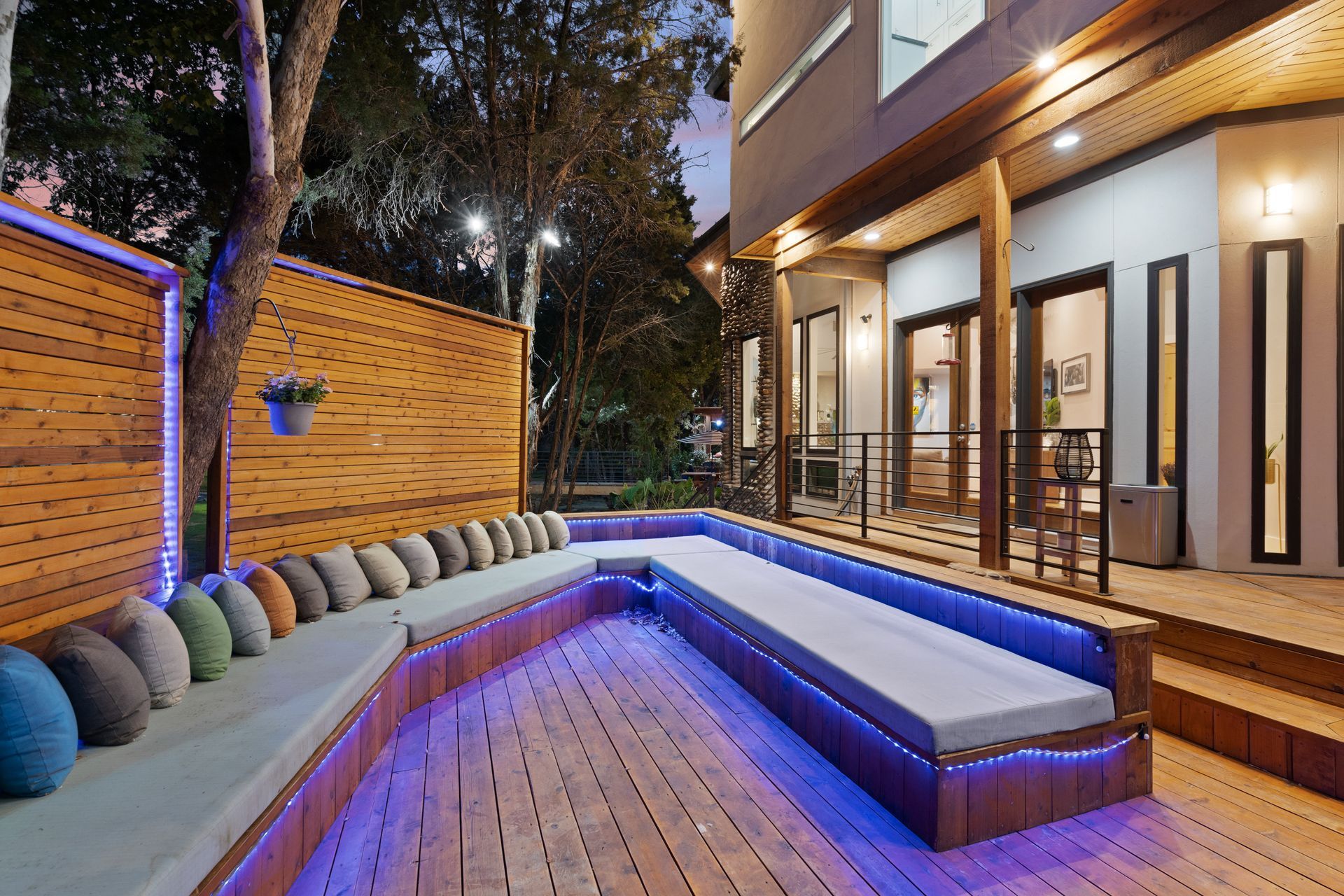 Stylish backyard with a wooden deck and outdoor sofa furniture, surrounded by lush greenery and decorated with potted plants and lights