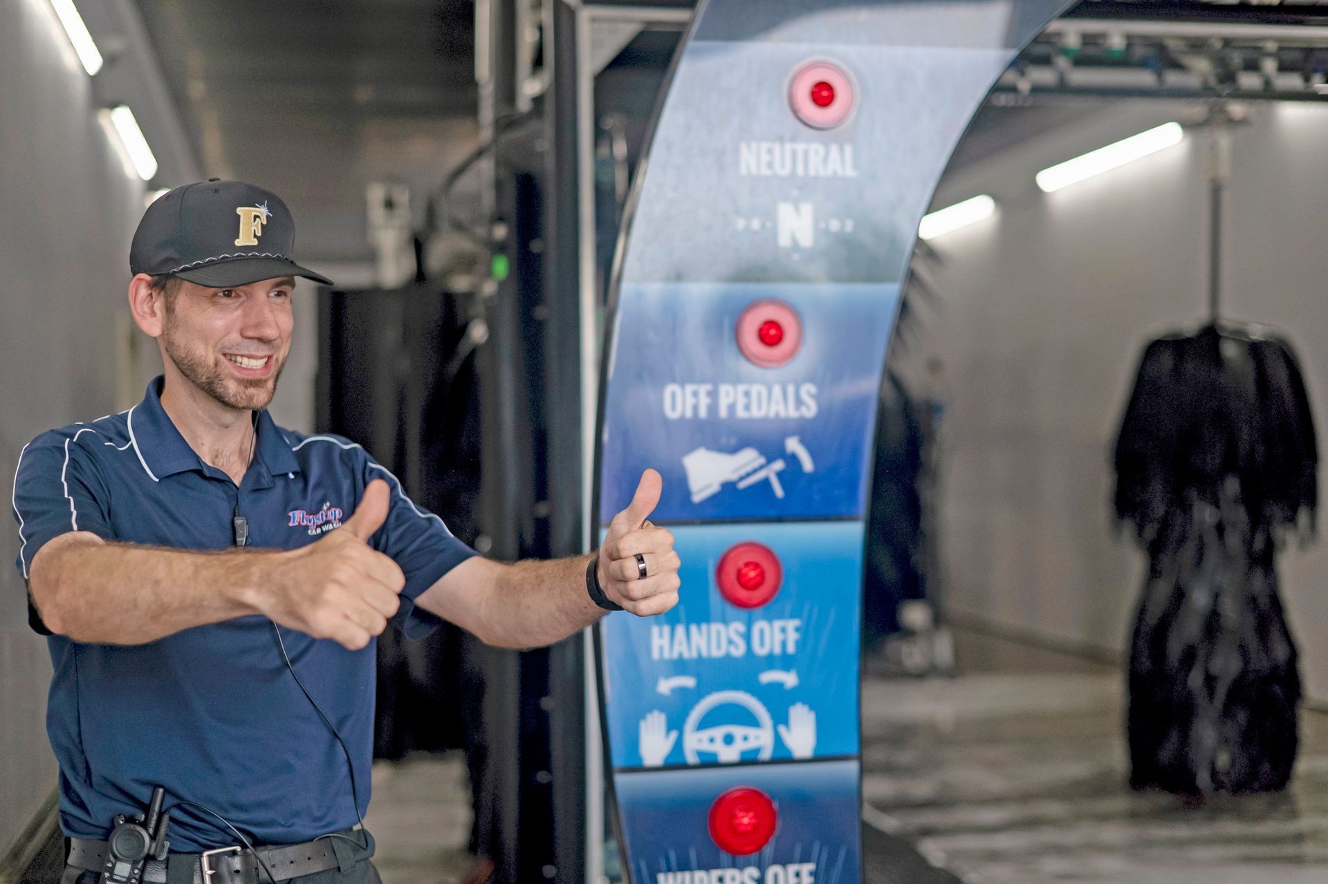 Man giving a thumbs-up beside a car wash sign with instructions in a tunnel-like wash bay