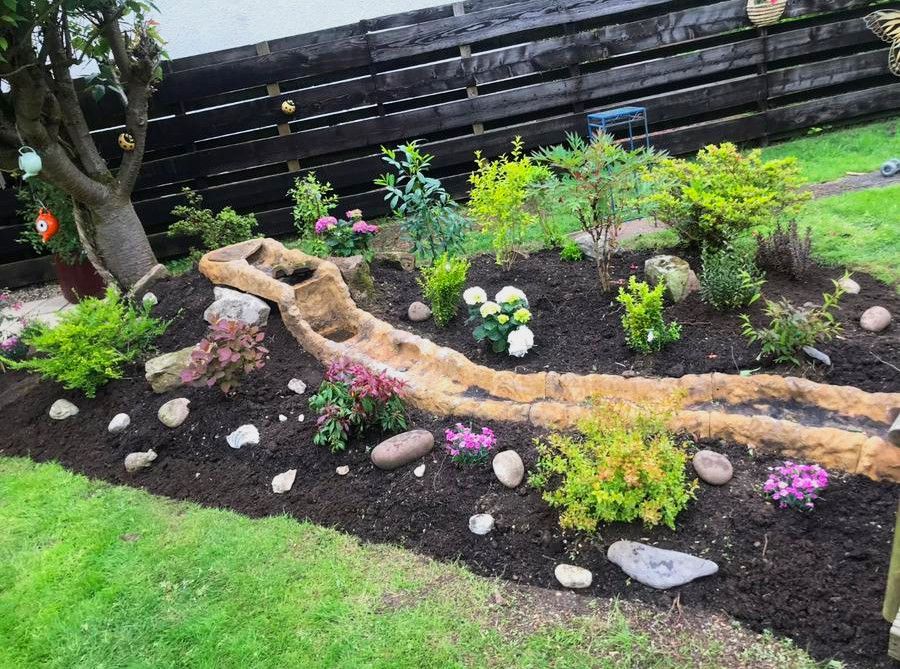 A garden with flowers and rocks and a wooden fence in the background.