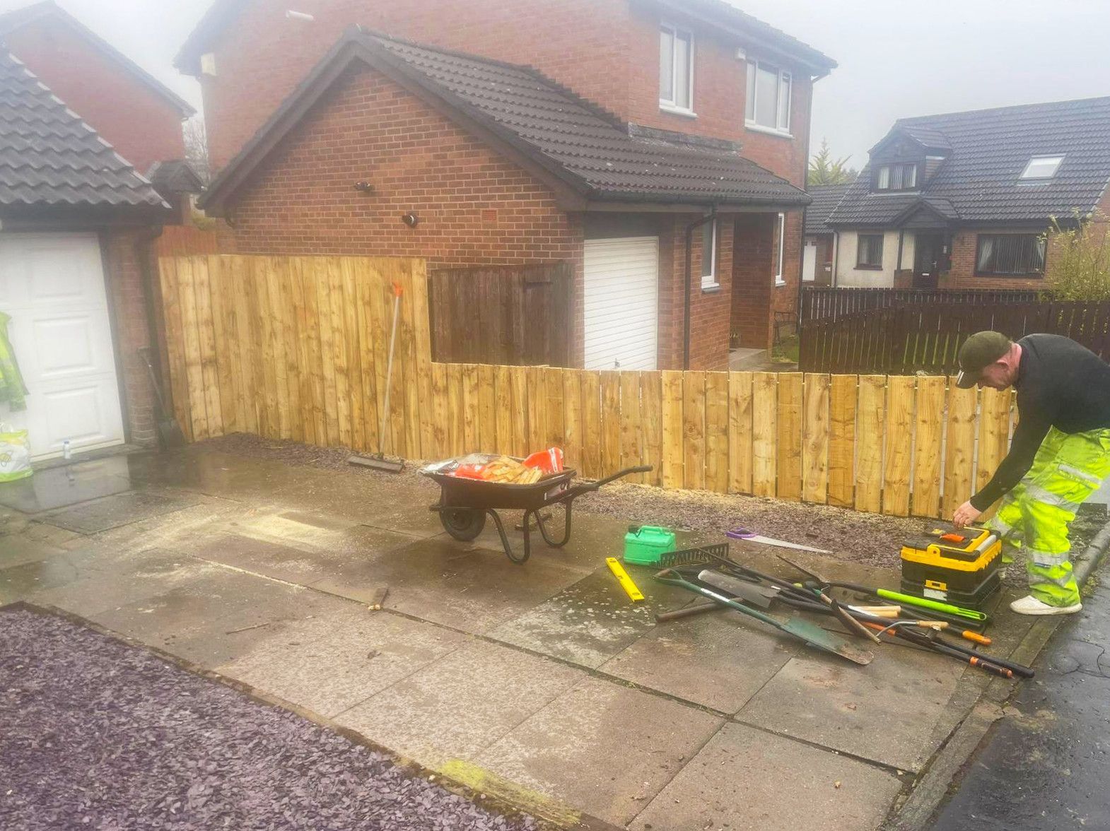 A man is working on a wooden fence in front of a house.