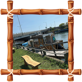 Harbor view with boats, bridge, and a wooden bench framed by a bamboo-style border