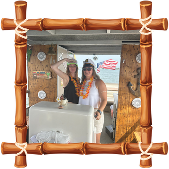 Two people posing in a tiki-style booth, with bamboo frame and tropical decor in the background.