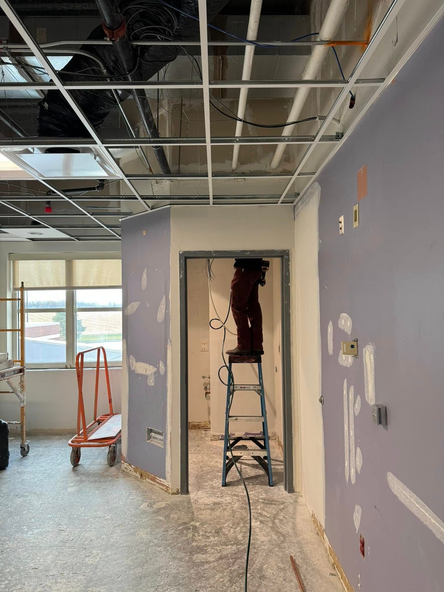 Partially renovated office hallway with exposed ceiling, purple walls, and a ladder in a doorway