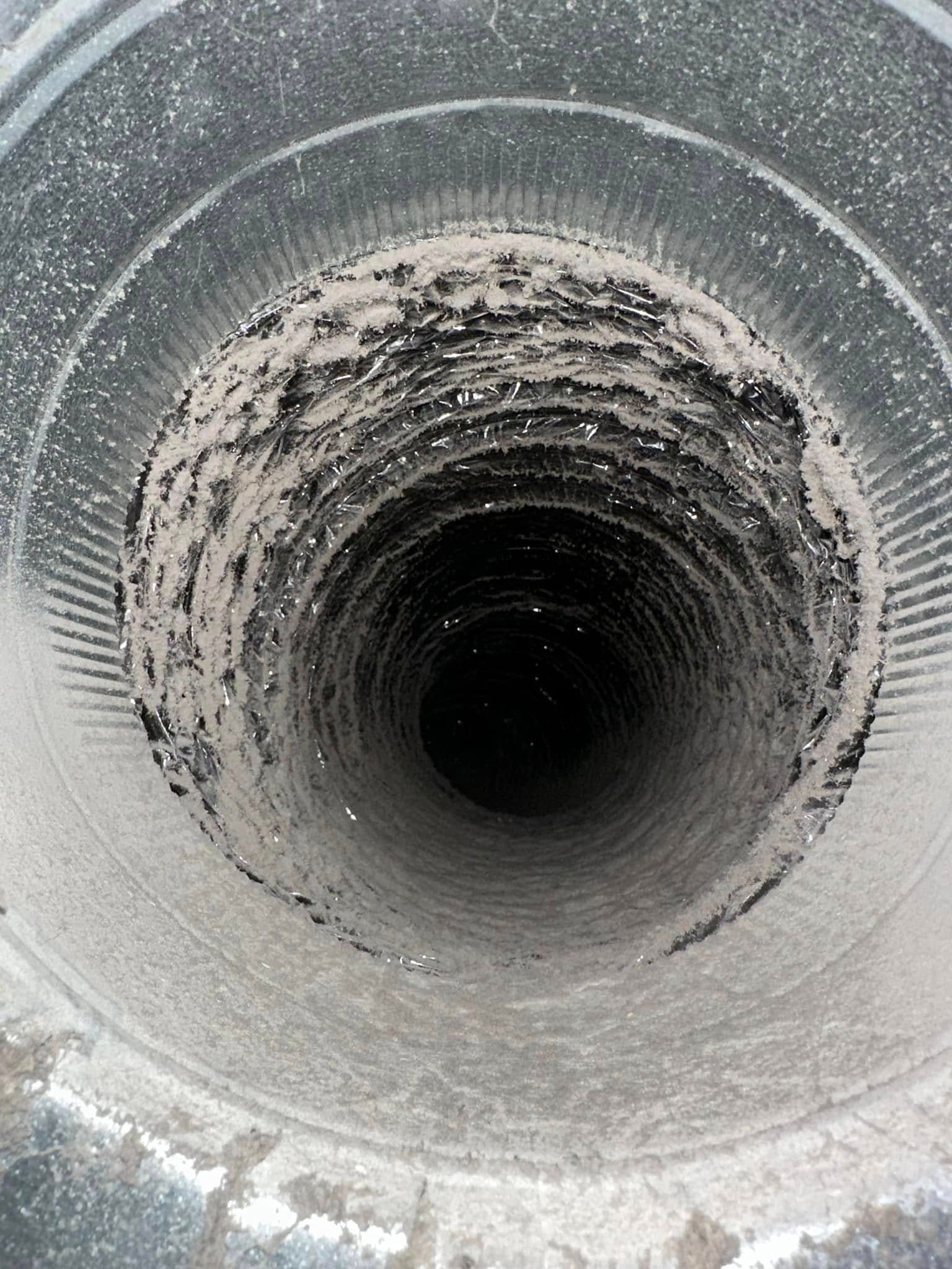 Close-up view down a dark, rough metal pipe with heavy white residue around the opening