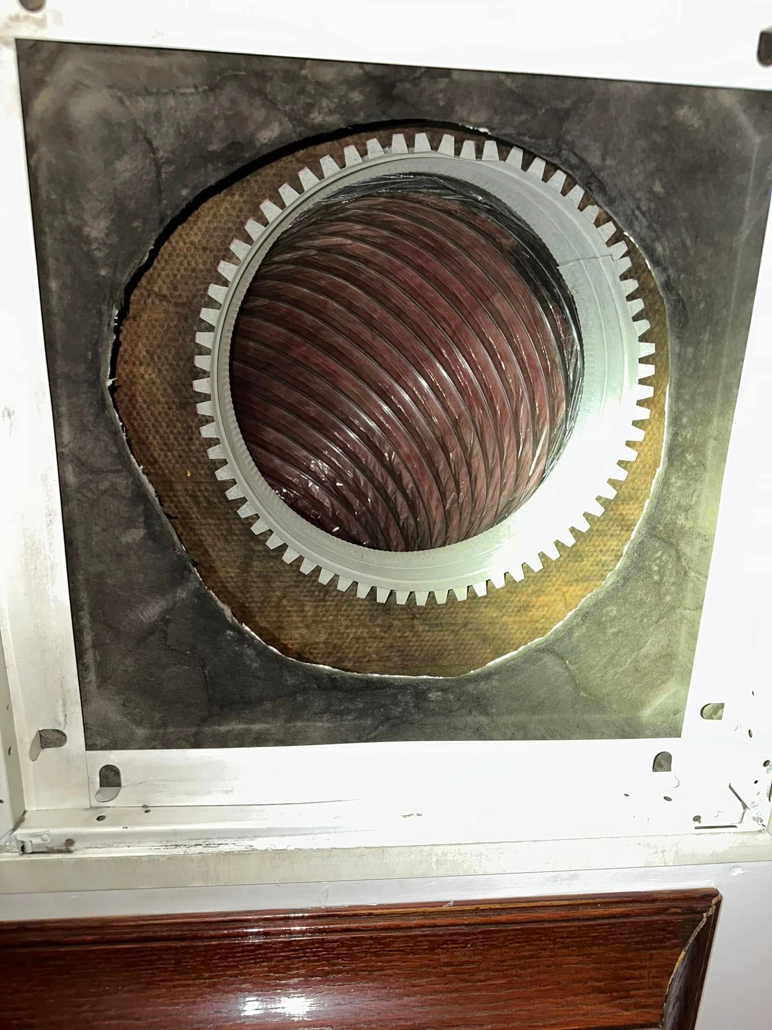 Close-up of a circular metal vent opening with a corrugated duct inside on a white appliance panel