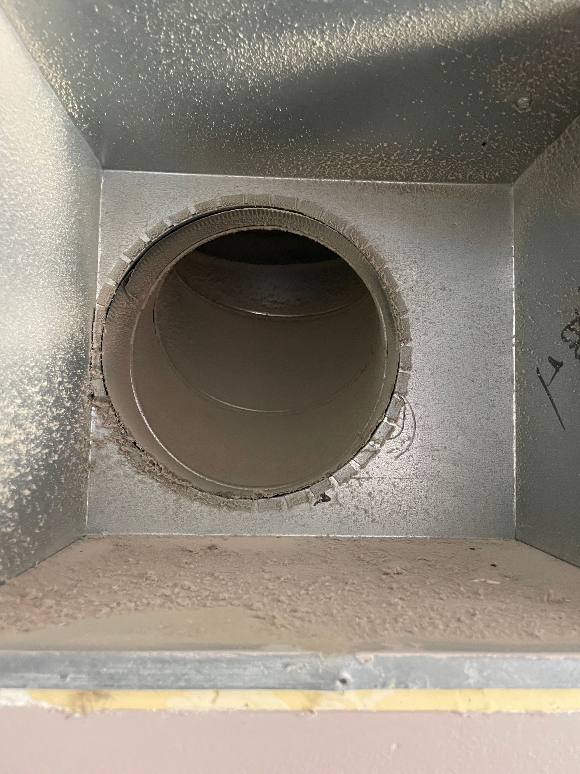 Close-up of a dusty metal duct opening inside a gray ventilation chamber
