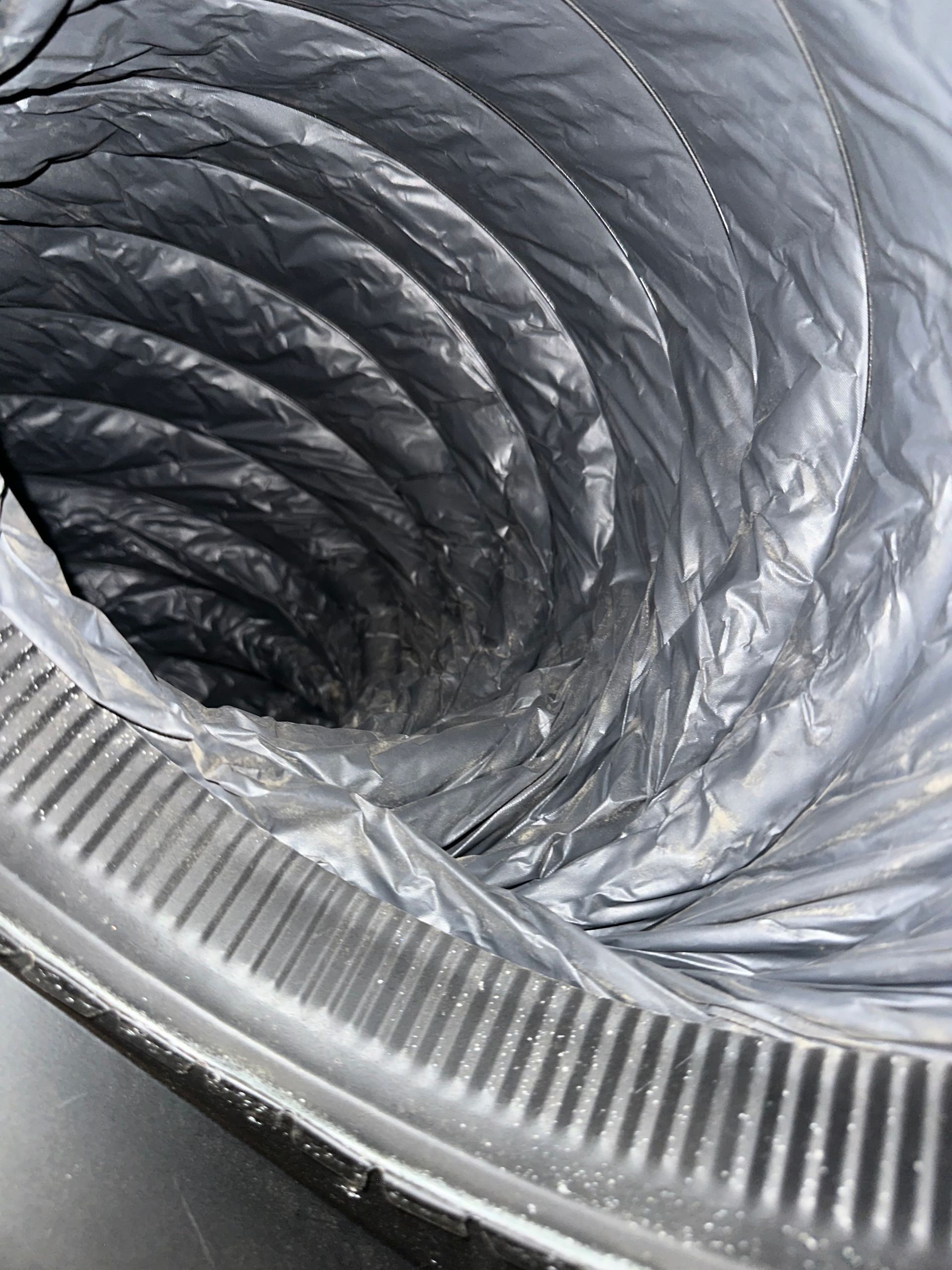Close-up of a coiled silver ventilation duct with a ridged metal rim