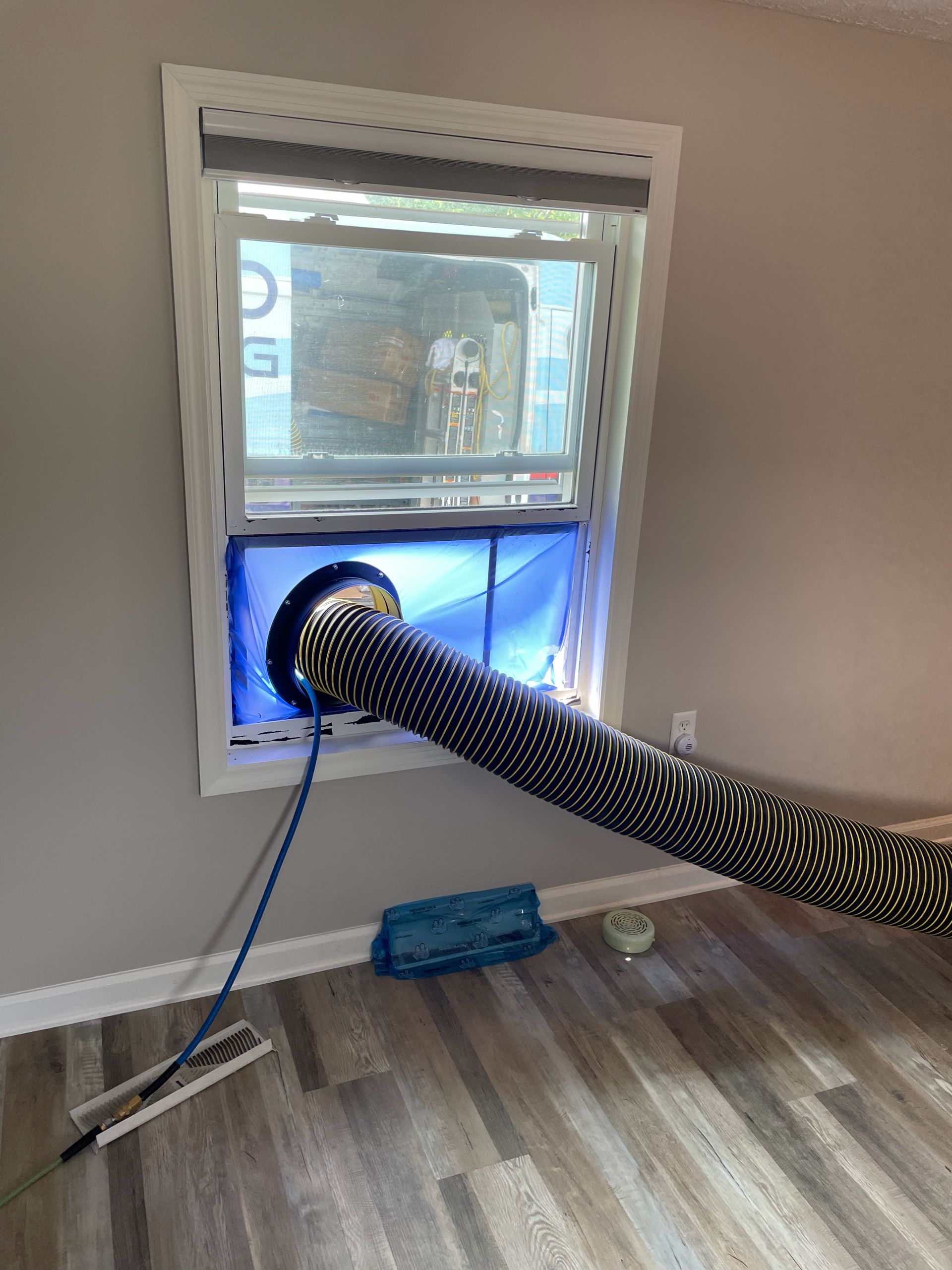 Portable vent hose through a window, with a blue panel and white frame in a room under repair