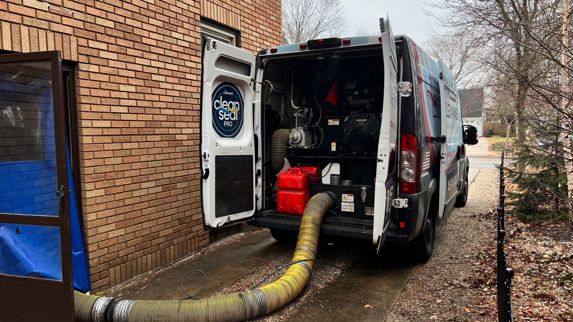 Fire truck with open rear doors and hose connected beside a brick building.
