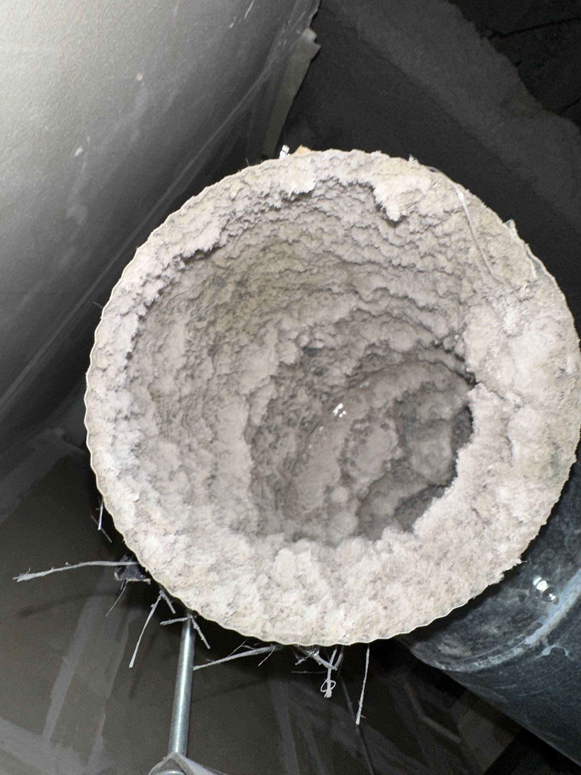 Close-up of a white, powdery buildup inside a circular pipe or duct opening