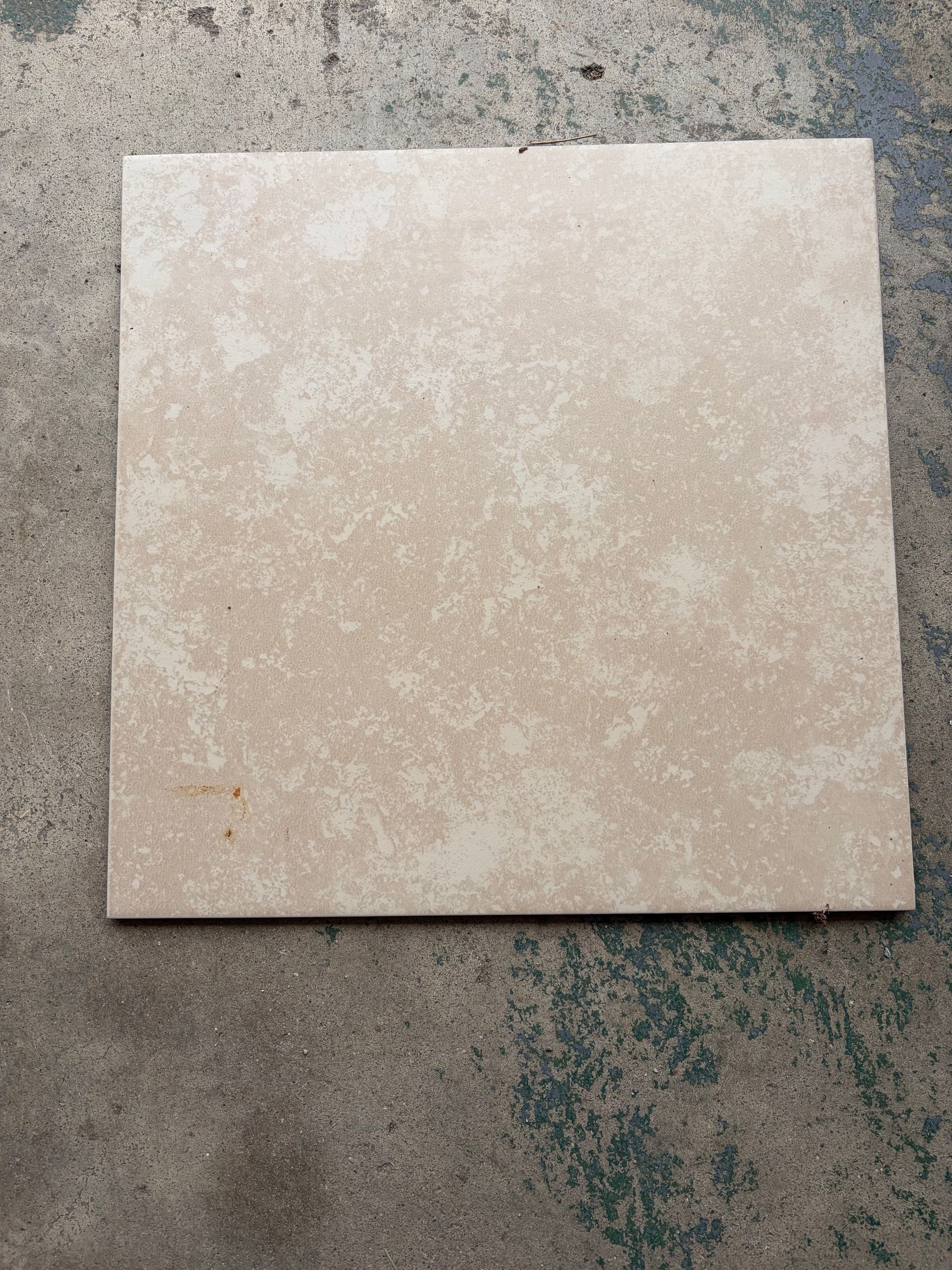 Square beige tile on a rough gray surface, viewed from above