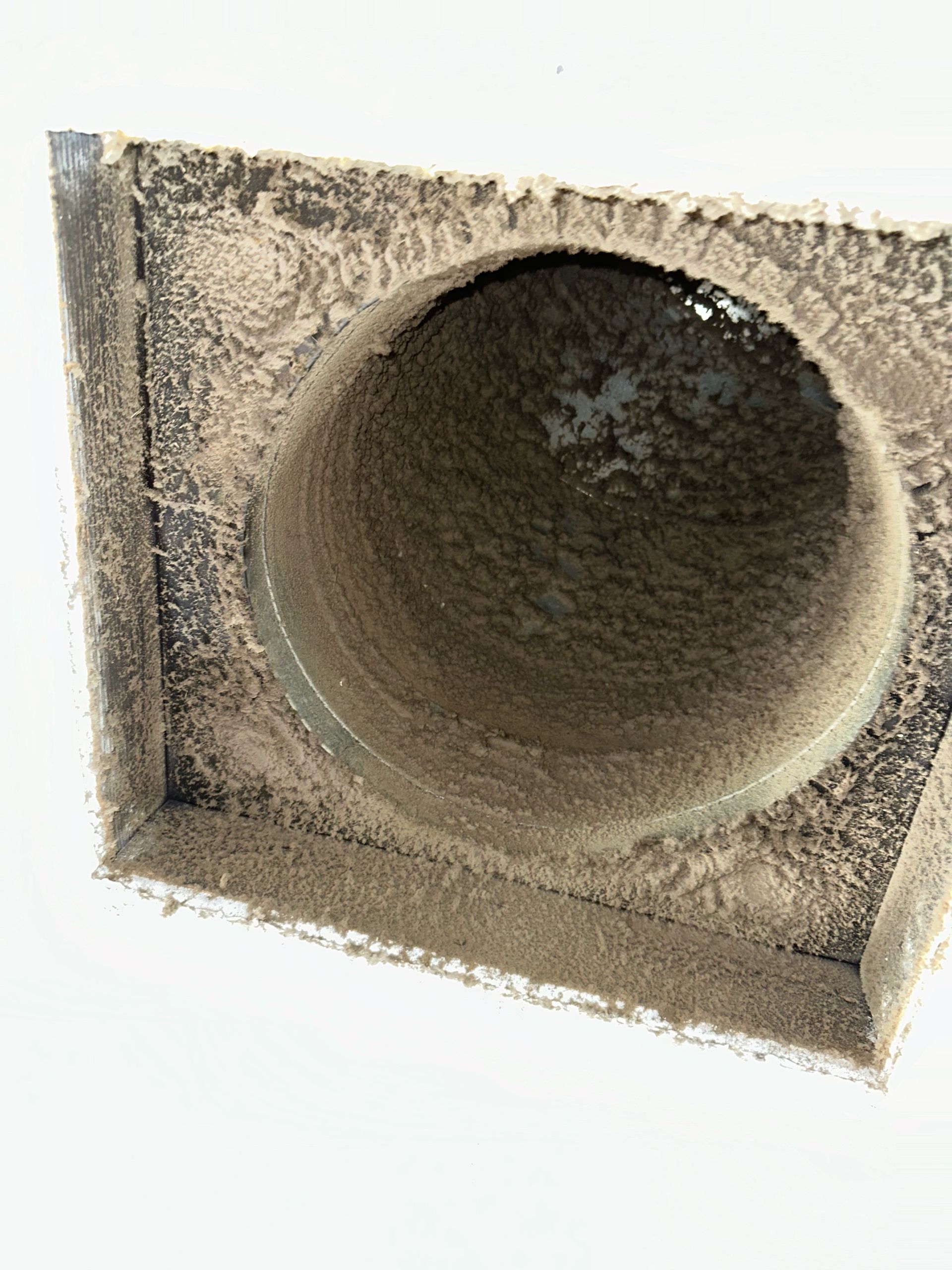 Dusty concrete vent opening in a beige wall, showing a round pipe interior.