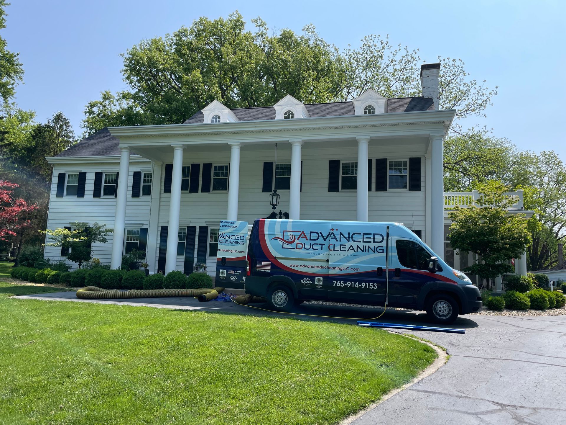 White colonial-style house with columns and a Dunkin’ delivery van parked in front.
