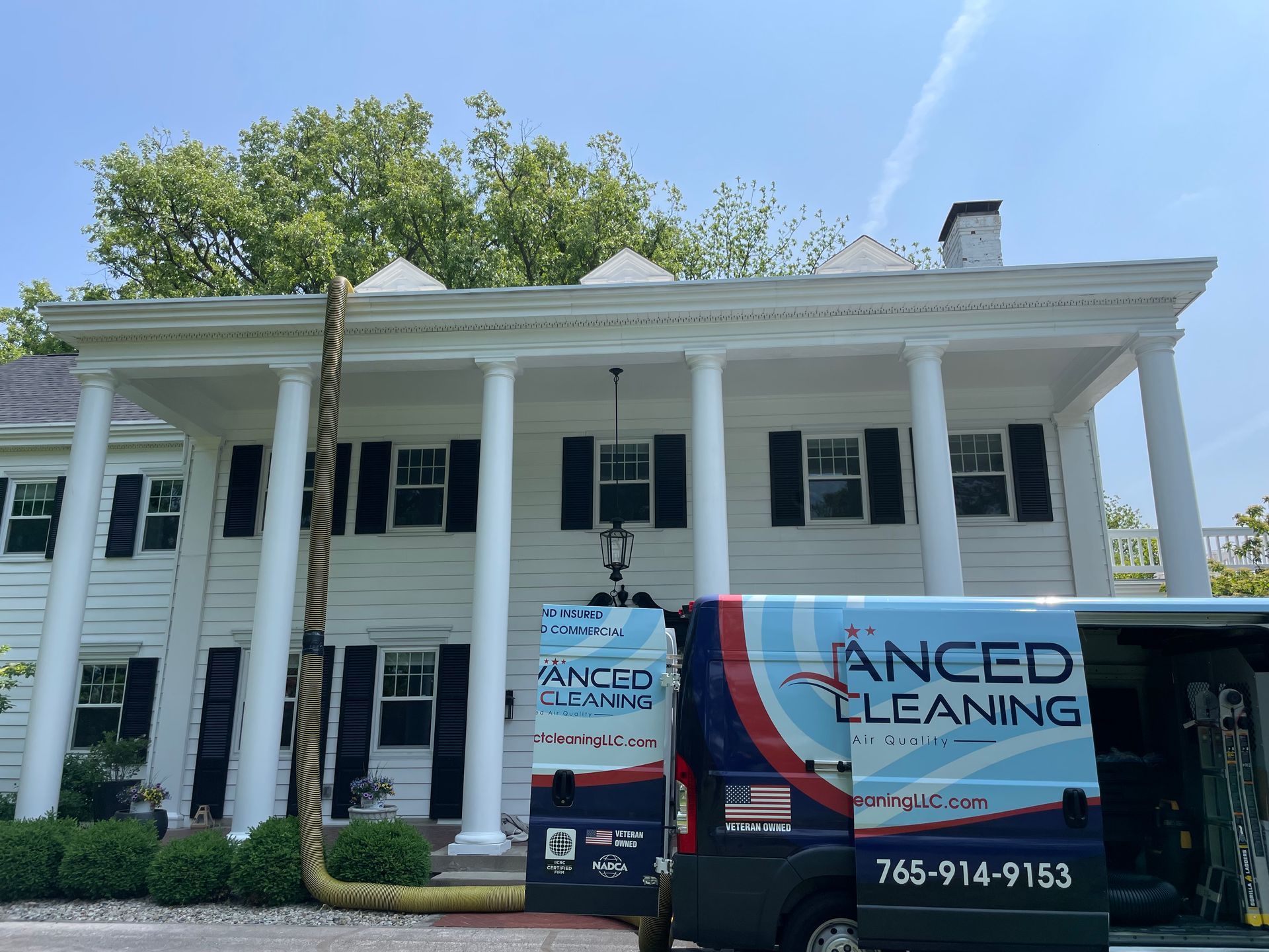 White house under renovation with large black-and-red exterior cleaning truck parked in front