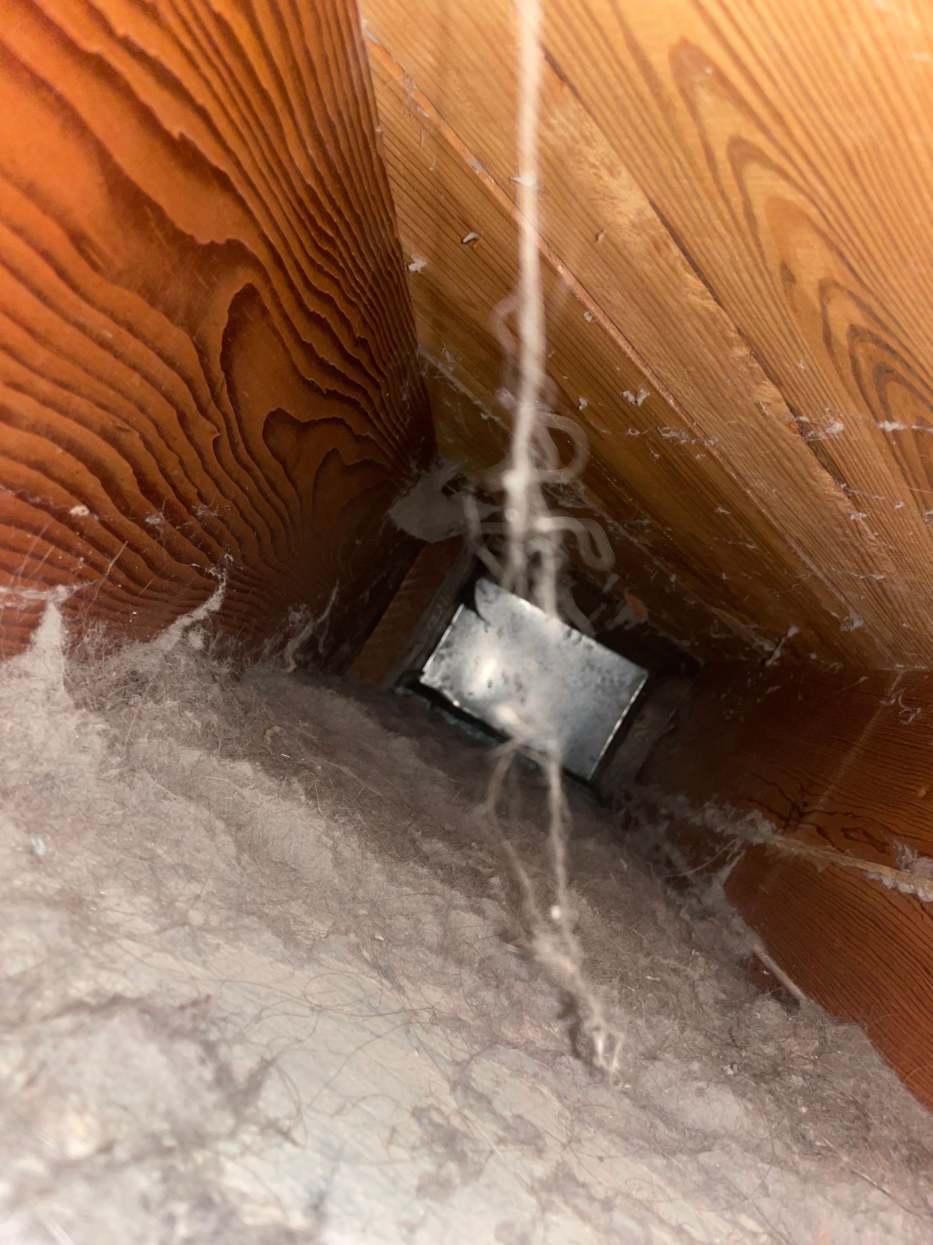 White cord hanging over a dusty wooden floor beside a small metal vent opening