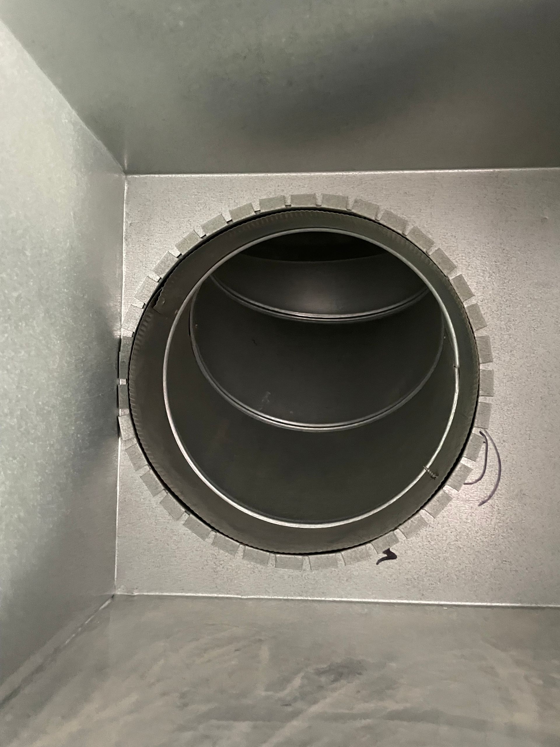 Close-up of a round metal ventilation duct inside a gray HVAC opening.
