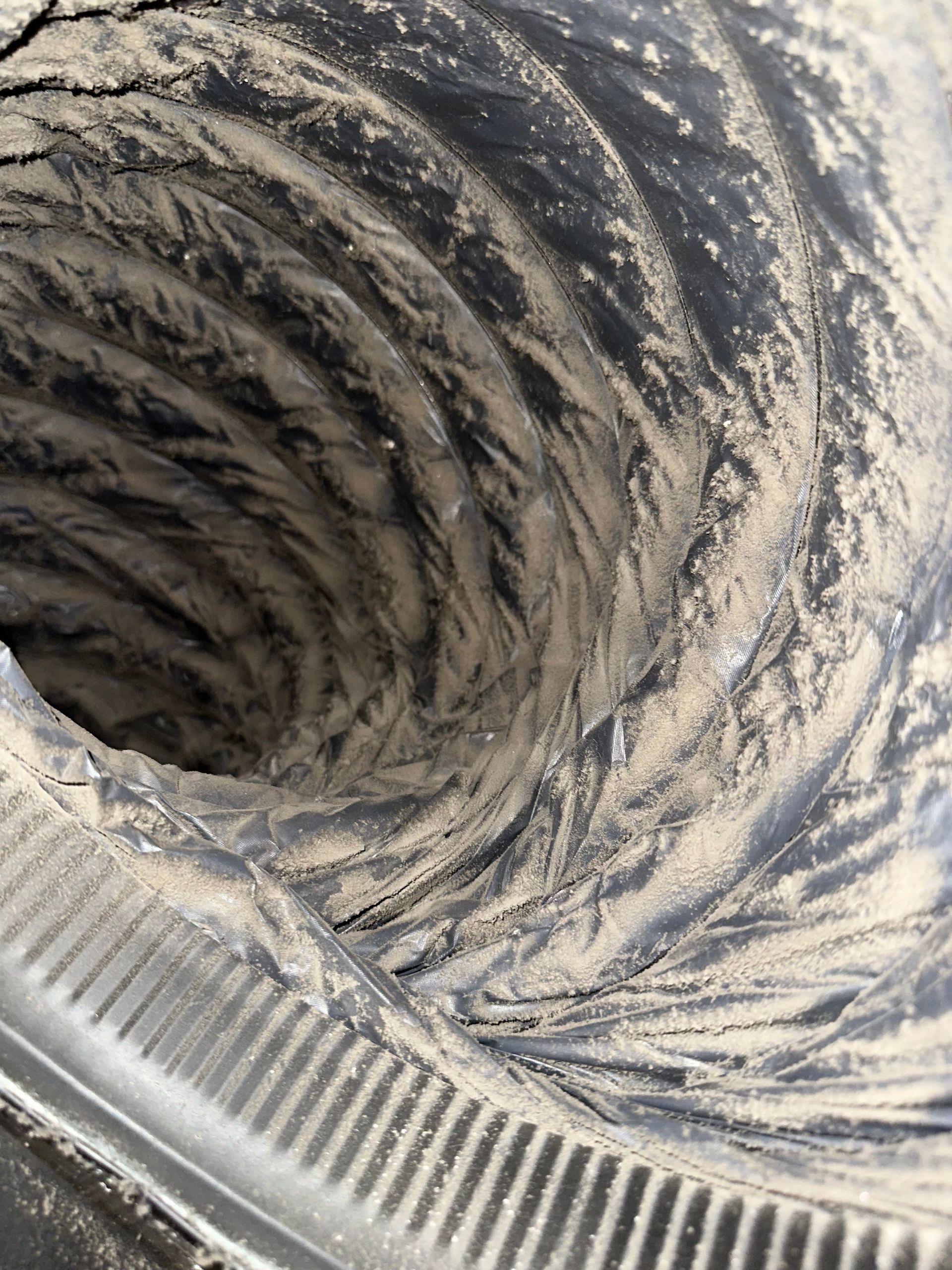 Close-up of a dusty air duct interior with a ribbed hose or vent opening.