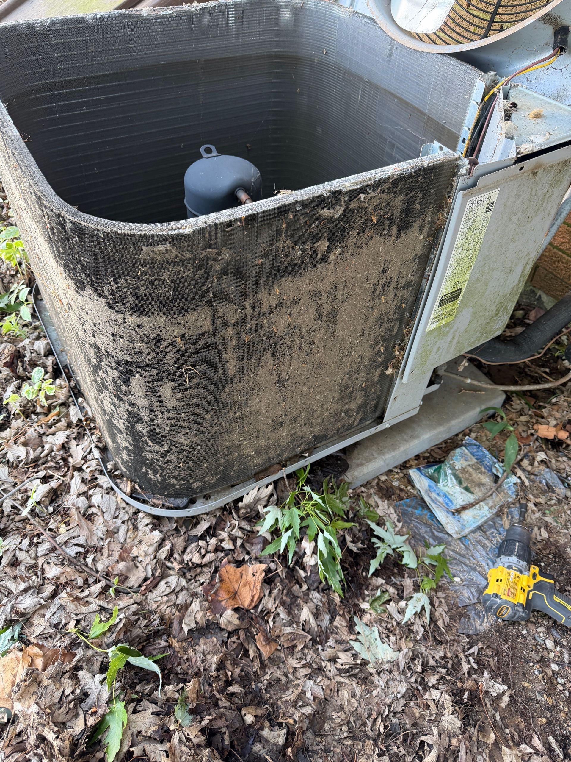 Dirty outdoor HVAC unit with a detached top cover and debris on the ground nearby