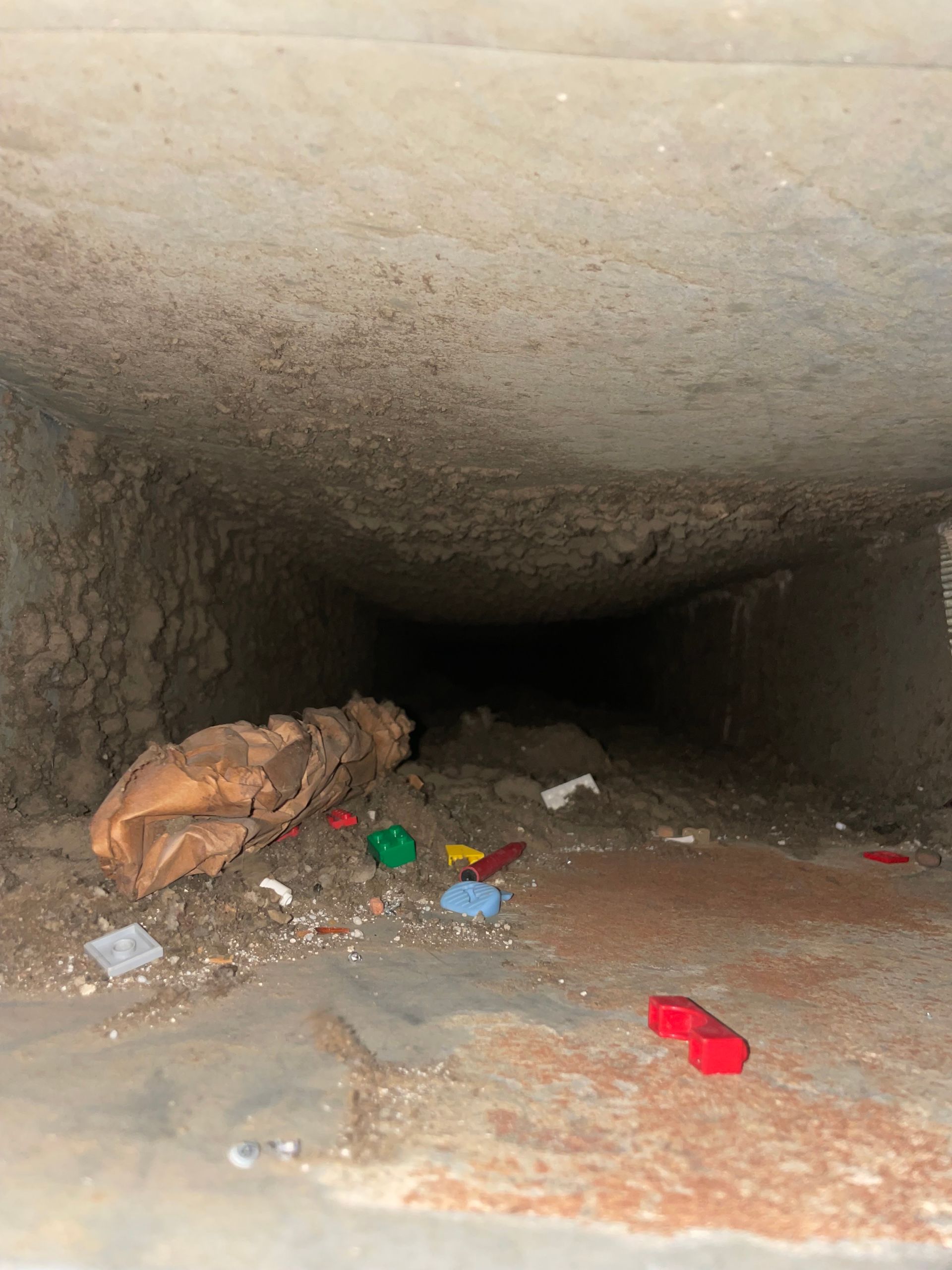Trash-strewn concrete tunnel with a large brown rat on the left side, disappearing into darkness